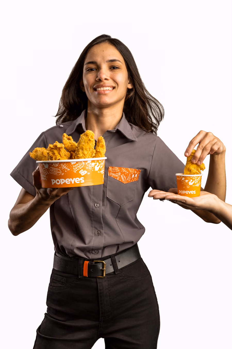 Colaboradora do Popeyes segurando um balde de frango; em seguida, a foto troca e aparece mordendo um pedaço de frango